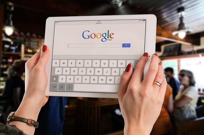 Mãos femininas segurando um tablet com página aberta no Google.